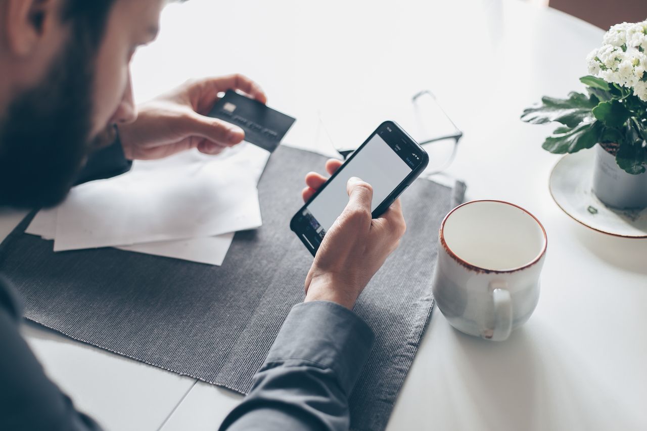 Man met smartphone en bankpas storten via iDEAL — KSA-casino mobiele betaling